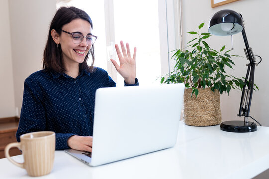 Woman waving during video call on laptop remote working