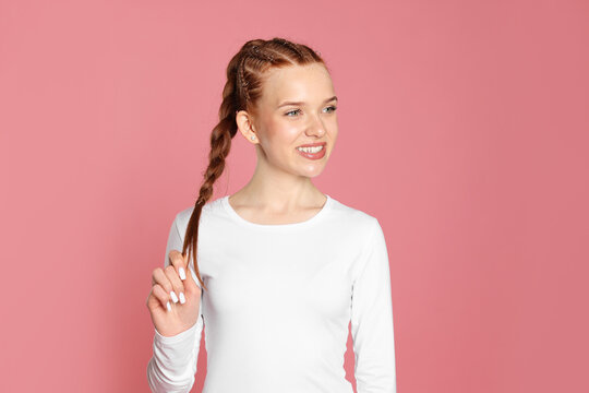 Smiling teenage girl with beautiful braids on pink background