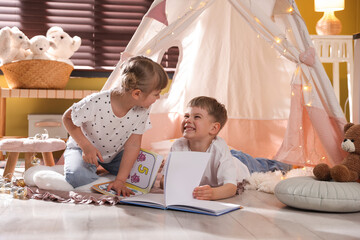Little girl and boy reading books near wigwam at home © New Africa