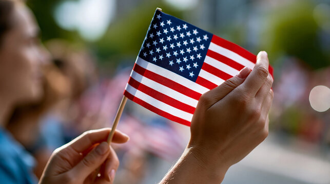 A close up of hands waves softly a bright patriotic flag at a calm holiday parade in soft daylight parade flag faceless detail softly defocused backdrop bright