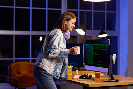 Happy female programmer with cup of coffee and computers working in office at night