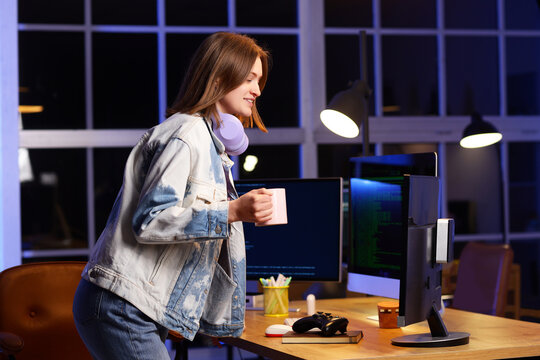 Happy female programmer with cup of coffee and computers working in office at night