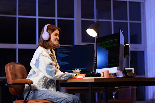 Happy female programmer with headphones and computers working in office at night