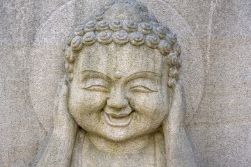 Obraz premium Smiling stone buddha statue covering ears at a korean temple.