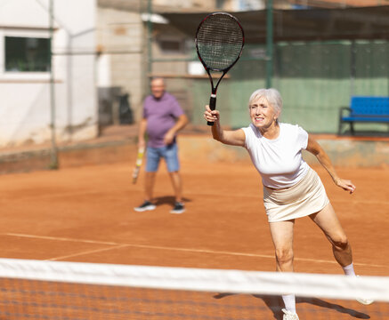 Sporty aged family during doubles match on indoor tennis court. Active lady hitting tennis ball with racket