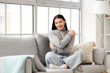 Obraz premium Beautiful young woman hugging herself on sofa at home