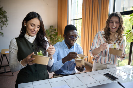 Diverse business colleagues enjoying a healthy office lunch together. Eating fresh salads from environmentally friendly containers during a cheerful work break