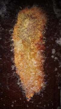 Close up view of cachopo, a traditional asturian dish, deep frying in bubbling hot oil. Golden brown breaded meat cooking in a pan