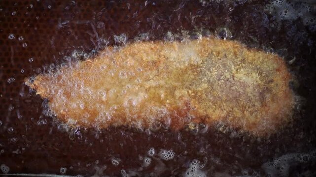 Delicious cachopo, a traditional asturian dish, deep frying in a pan with bubbling hot oil. Crispy, golden brown breaded veal steak