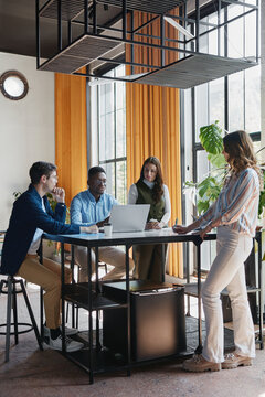 Diverse business team collaborating during a casual meeting in a modern coworking office, sharing ideas and working together on a laptop for a successful project outcome