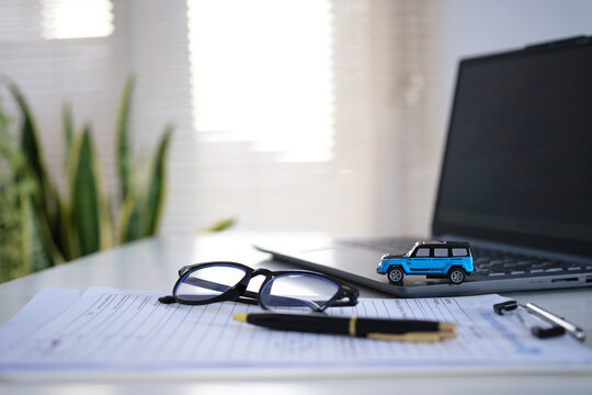 A miniature car on a laptop and documents on a desk. Planning for managing transportation costs. A car insurance business concept, a savings account for buying and selling with taxes, and a loan for a