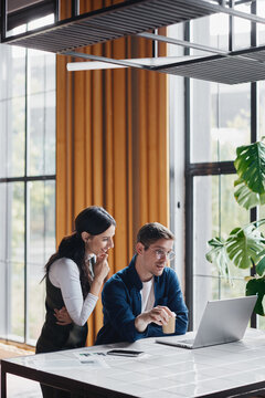 Professional colleagues collaborating on a laptop in a modern office, discussing a project and analyzing data while sharing ideas and strategy for solutions