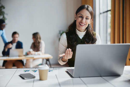 Business woman participating in a successful online meeting, interacting with colleagues during a video call, using a laptop in a modern office environment