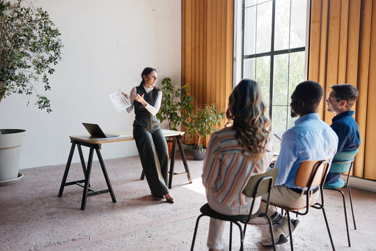 Female speaker presenting business strategy and innovative ideas to a diverse audience, fostering collaboration and knowledge sharing during an office meeting or workshop