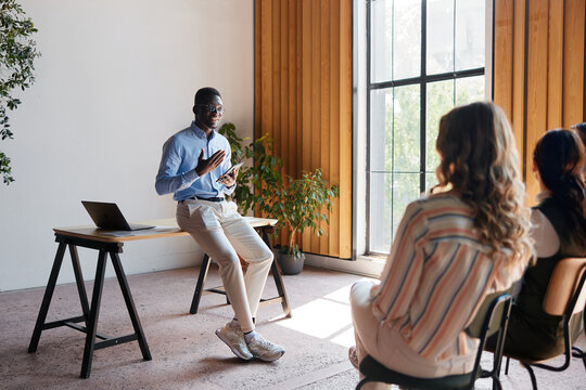 Diverse business leader presenting to a small group in a modern office, communicating ideas and providing executive training during a corporate meeting or workshop