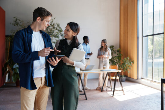 Business colleagues collaborating, discussing new project ideas, and sharing insights while looking at a tablet in a modern office, focusing on teamwork and innovation