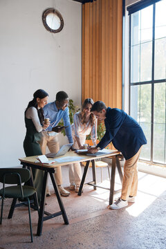 Diverse business team collaborating on project in modern office, using laptop and documents, discussing strategy during a focused creative meeting
