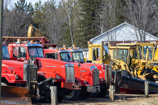 Quebec, Canada, 24 April 2026 : Red Western Star, Autocar, and Kenworth snowplow trucks are parked with yellow heavy equipment.