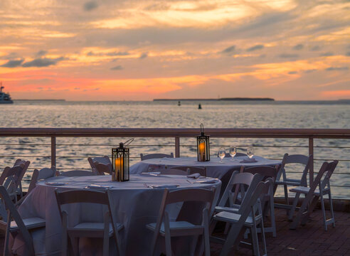 Round banquet tables with white tablecloths and chairs stand on the outdoor Key West pier during the colorful evening sunset.