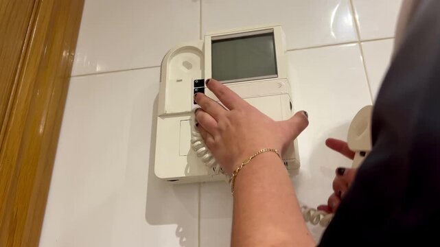 Woman answering video door phone, pressing button and picking up handset