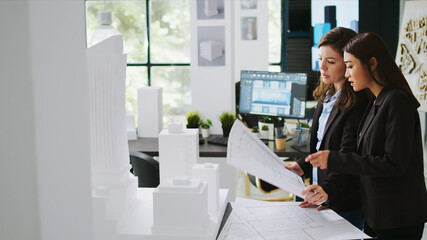 Naklejka premium Architects team studying 3D printed building model in office, looking at scale and outline to reveal floor plan measurements, creative agency employees working with architectural blueprints