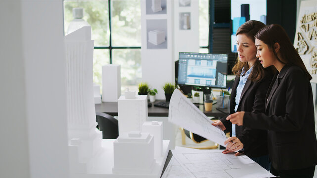 Architects team studying 3D printed building model in office, looking at scale and outline to reveal floor plan measurements, creative agency employees working with architectural blueprints