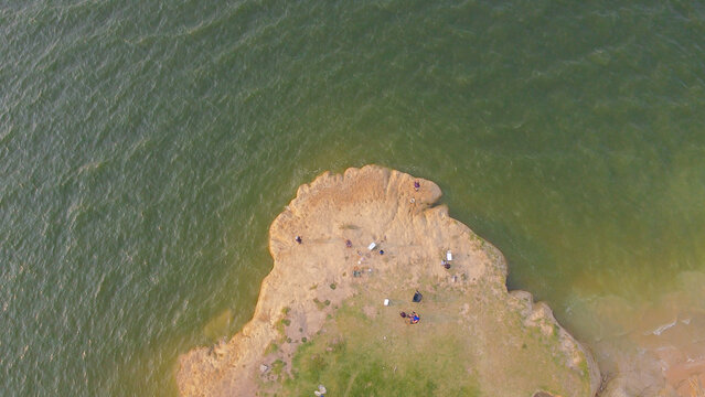 Lake Lavon peninsula south of CR 952 near Princeton showing spaced anglers on grassy exposed soil point. Varied earth textures, scattered items, shifting water hues frame scene, Texas