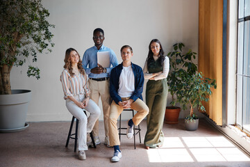 Fototapeta premium Four smiling young diverse professionals are posing for a portrait in a bright contemporary office, representing teamwork, collaboration, and a successful business environment