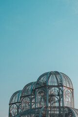 Naklejka premium Glass and Iron Greenhouse Domes at Curitiba Botanical Garden Against Blue Sky