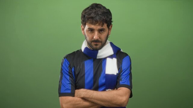 Man in blue and black striped football jersey and scarf with forearms crossed, head down in studio; disappointment.