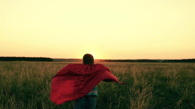 Superhero, child son, plays in summer field sunset. Happy family picnic outdoors. Kid boy dreams becoming superhero runs in red cape park sunset. Family games, picnic, nature, holiday. Kid superhero