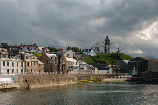 Macduff harbor town under dramatic cloudy sky showing traditional Scottish buildings and prominent church on a green hill