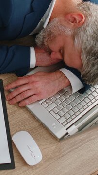 Bored sleepy mature old businessman programmer software developer in formal wear suit falling asleep after routine work on laptop at office desk. Exhausted tired freelancer workaholic man. Overworked