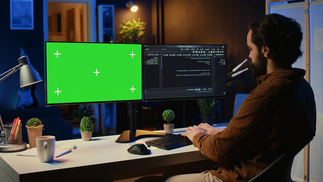 Programmer typing complex code on green screen computer in neon lit home office, developing software application.