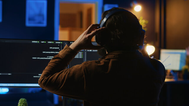 Engineer wearing headphones while using coding to fortify security, remotely working for IT company. Software expert listening music and upgrading binary code scripts on computer.