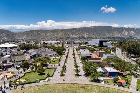 People Walk Through Park in Ambato, Ecuador During Sunny Day With Mountains in Background and Clear Blue Sky