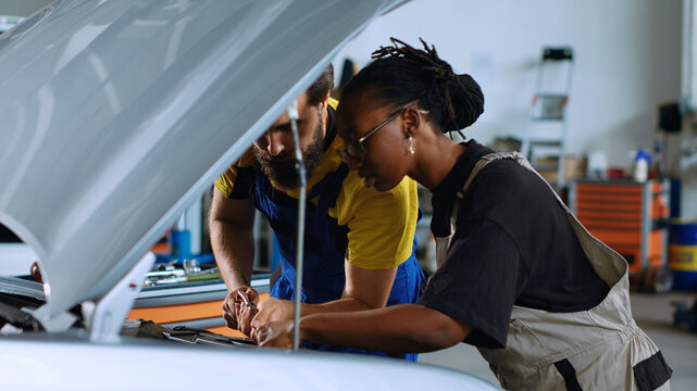 Coworking technicians in car service using torque wrench to fix damaged automobile, with man and woman in repair shop servicing broken vehicle, checking for faulty transmission using professional.