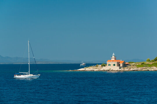 Yacht passing picturesque Pokonji Dol Lighthouse on a small islet in the Pakleni Islands archipelago near Hvar, Croatia