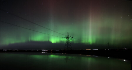 Fototapeta premium Aurora Borealis Behind Power Transmission Tower at Night Reflected in Calm Water
