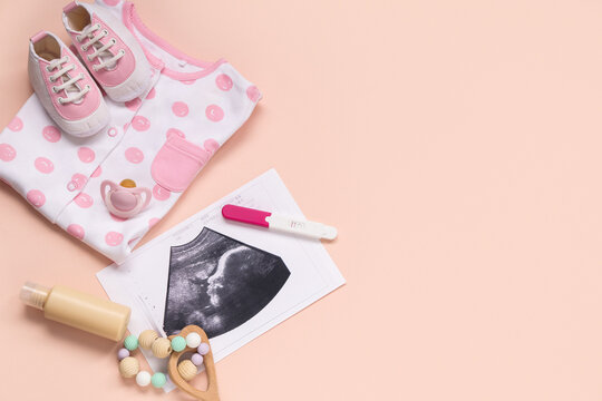 Composition with baby clothes, sonogram image, pregnancy test and rattle on pink background