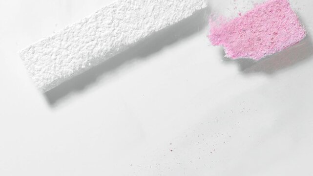 Slow-motion frame of red, pink, and white loose powder sifted through a three-stripe stencil on a transparent surface, blown away by air stream on pale grey background | Marketing campaign for blush