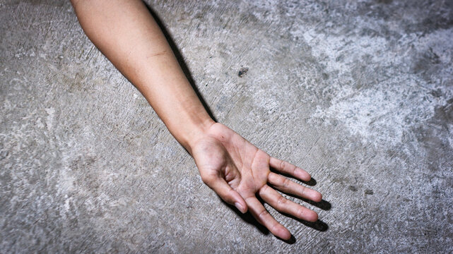 A crime scene concept showing a human hand lying lifeless  or dead body on the concrete floor, with the body covered by a white cloth fabric.murder concept.