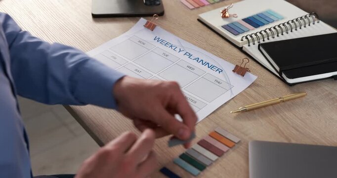 Man using weekly planner at wooden desk indoors, closeup