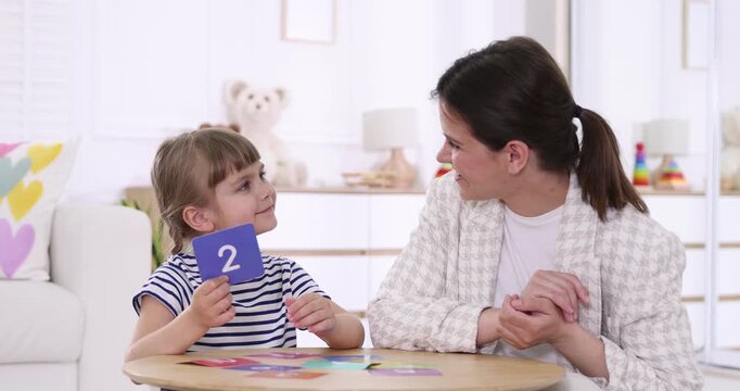 Speech therapist teaching girl numbers with colorful cards at wooden table indoors