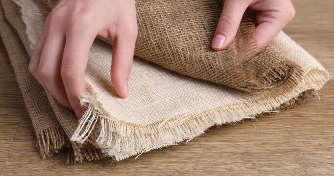 Woman with folded burlap fabrics at wooden table, closeup