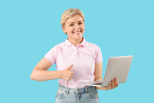 Happy young female programmer with laptop showing thumb-up gesture on blue background