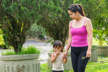 Obraz premium Latina mother walking with her daughter as the child eats a snack during a park stroll
