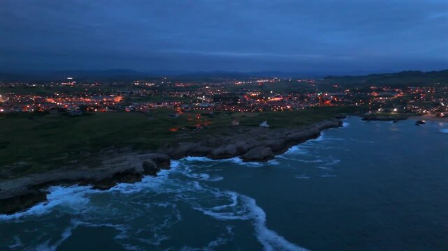 Drone approach toward a sheltered bay and illuminated seaside town in Santander Spain at dusk