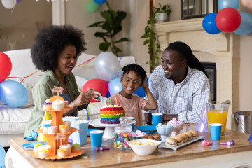 Obraz premium African American family celebrating birthday with rainbow cake and balloons in living room