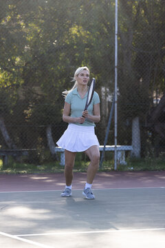 Woman tennis player standing holding racket on hard court midcourt wearing polo and skirt
